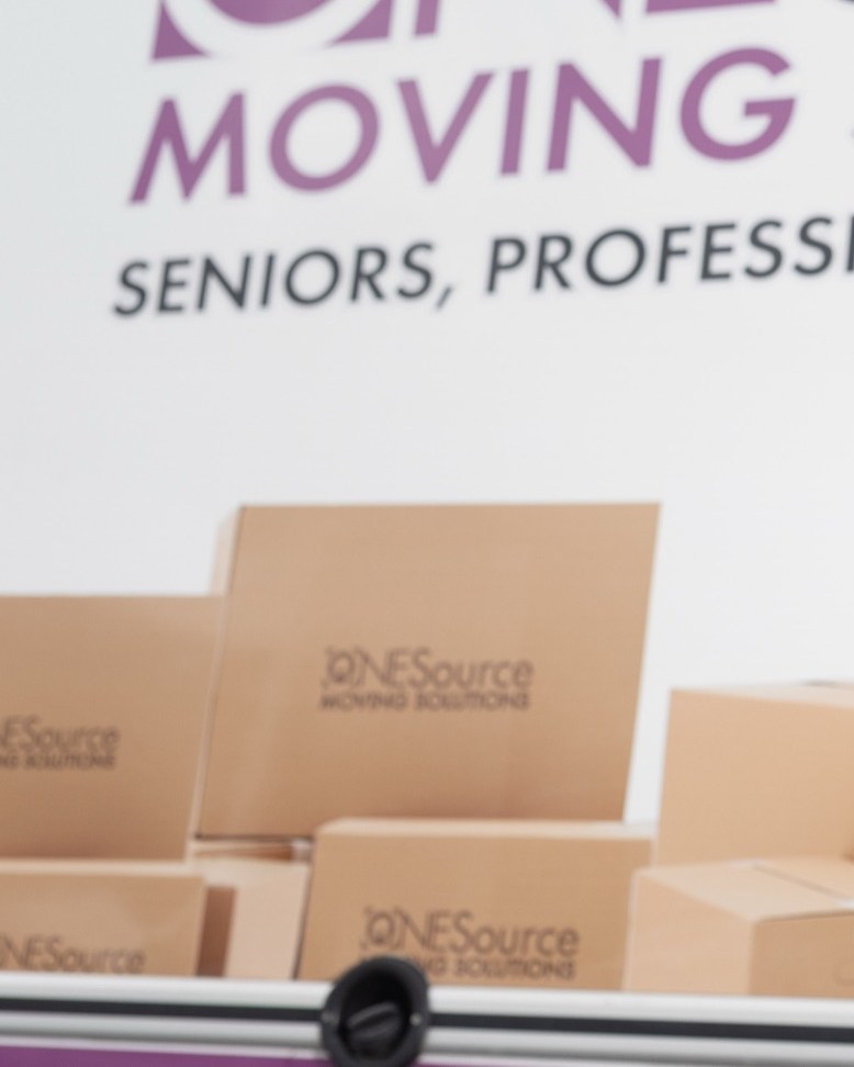 Stacked ONESource branded moving boxes in front of the company banner